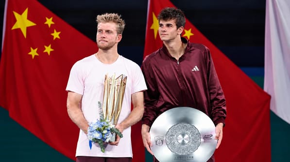 O tenista espanhol Alejandro Davidovich Fokina, de camisa rosa-clara e faixa na cabeça, grita de punhos cerrados com a raquete na mão, diante de um painel verde do torneio