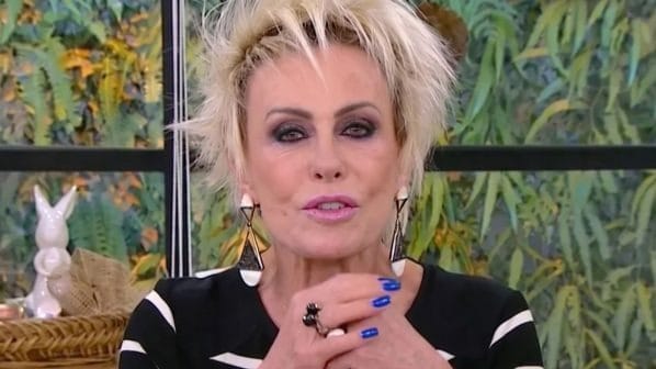 Ana Maria Braga, de cabelo loiro curto e blusa listrada de preto e branco, fala com as mãos unidas no estúdio do Mais Você