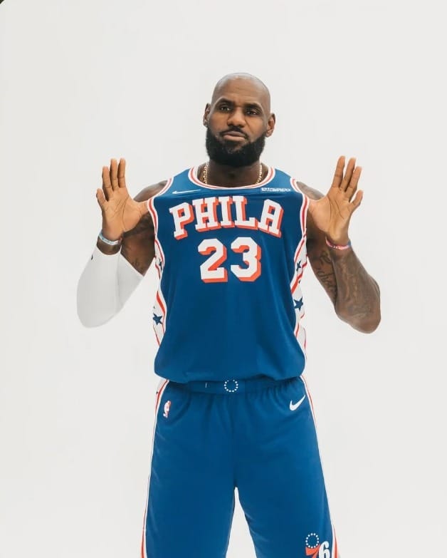 LeBron James posa com a camisa 23 azul do Philadelphia 76ers, com as mãos abertas na altura do peito