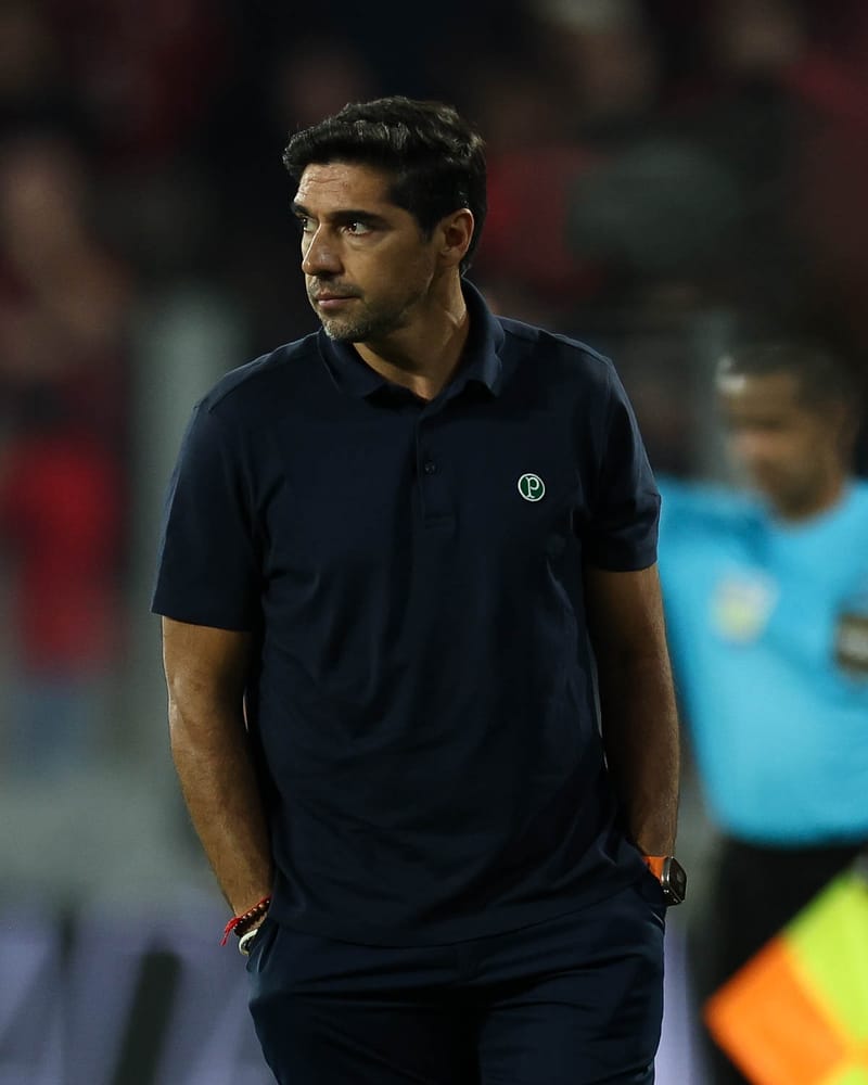 Abel Ferreira, técnico do Palmeiras, de polo azul-marinho com o escudo do clube e mãos nos bolsos, olha para o lado à beira do gramado
