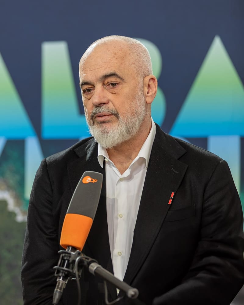 O primeiro-ministro da Albânia, Edi Rama, de barba grisalha e paletó escuro, fala diante de um microfone