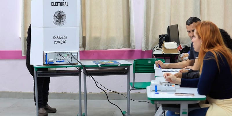 Cabine de votação ao lado de mesas com mesários, em uma seção eleitoral