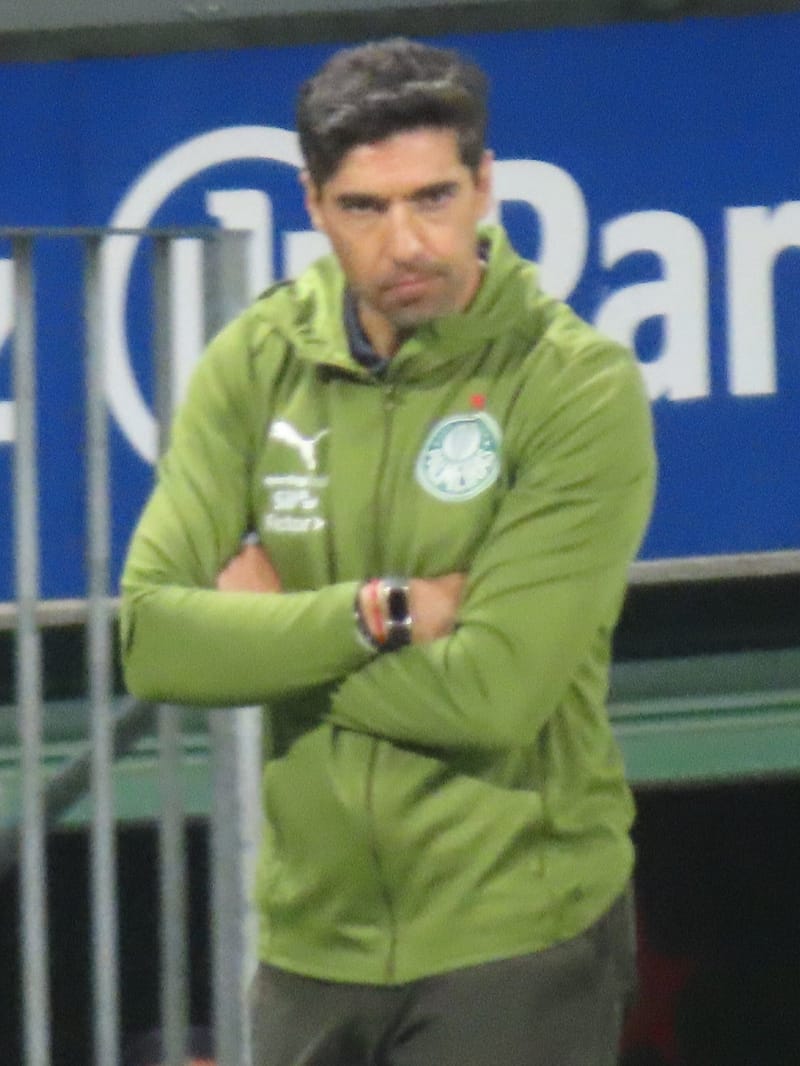 Abel Ferreira, de agasalho verde do Palmeiras, de braços cruzados e expressão séria, à beira do campo