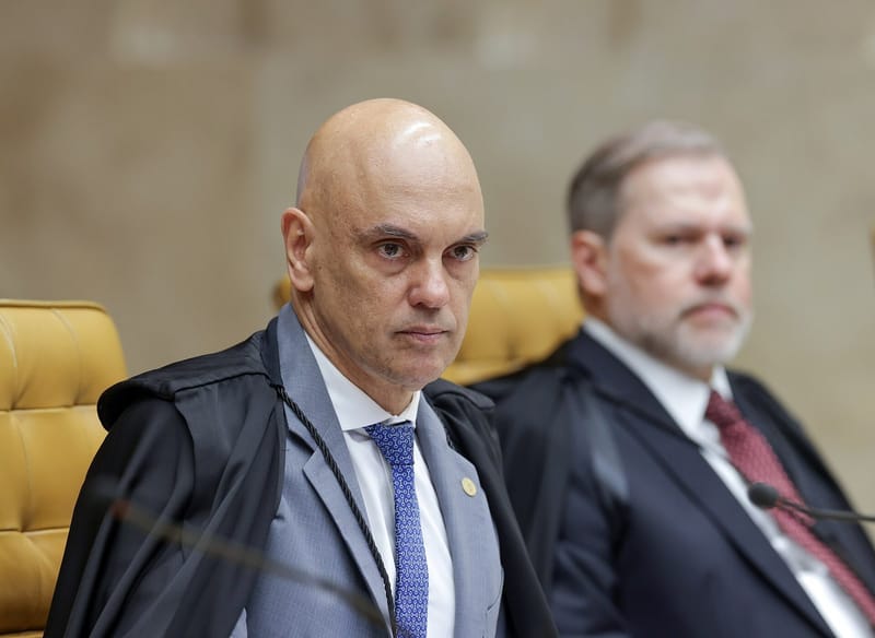 O ministro Alexandre de Moraes, de toga preta e gravata azul, sentado no plenário do STF, olha de lado com expressão séria