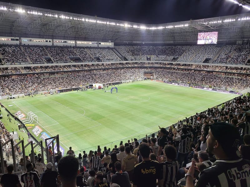 Gramado e arquibancadas da Arena MRV à noite, com a torcida atleticana em primeiro plano