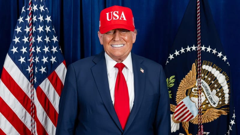 O presidente Donald Trump, de terno azul, gravata vermelha e boné vermelho escrito USA, posa diante das bandeiras dos Estados Unidos e da Presidência