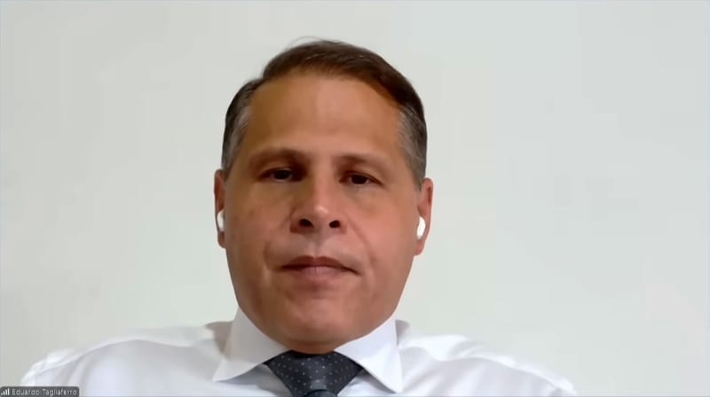 Eduardo Tagliaferro, de camisa branca e gravata escura, fala por videoconferência diante de uma parede clara