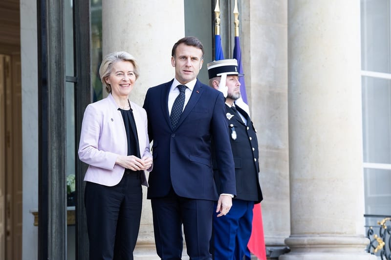 Emmanuel Macron, de terno azul-marinho, ao lado de Ursula von der Leyen, de blazer claro, diante das colunas do Palácio do Eliseu e de um guarda de gala