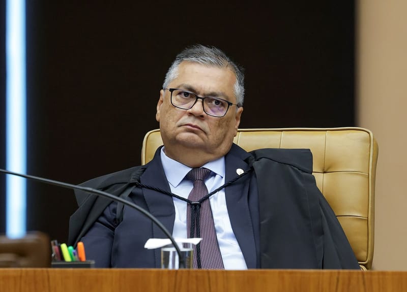 Flávio Dino, de óculos, toga e gravata vinho, sentado na cadeira do plenário do STF com o olhar para cima