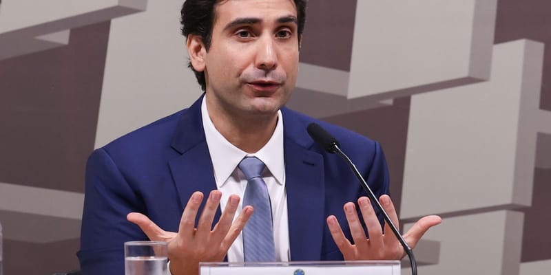 Gabriel Galípolo, de terno azul-marinho e gravata azul, gesticula com as duas mãos abertas diante de um microfone