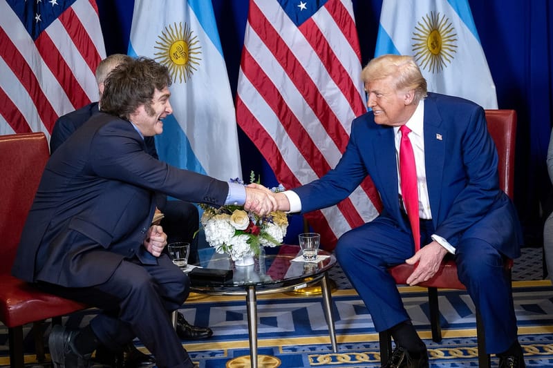 Javier Milei, à esquerda, e Donald Trump, à direita, trocam um aperto de mão sentados diante de bandeiras da Argentina e dos Estados Unidos