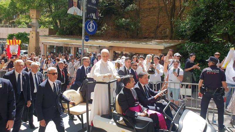O papa Leão XIV, de branco, acena de um carrinho elétrico cercado por seguranças e fiéis em uma rua da abadia de Montserrat