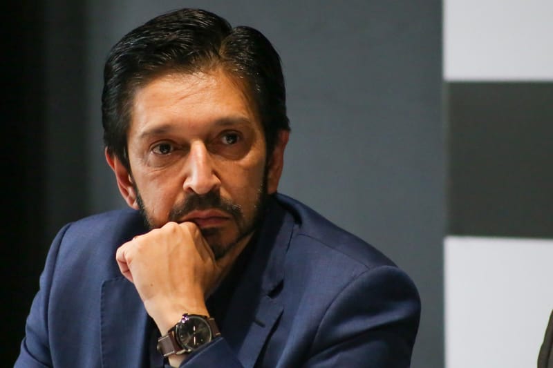 Ricardo Nunes, de barba curta e terno escuro, apoia o queixo na mão e olha para a frente, com expressão séria
