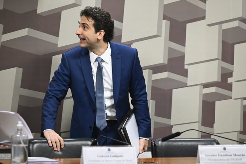 Gabriel Galípolo, de terno azul, em pé diante da cadeira numa reunião de comissão do Senado