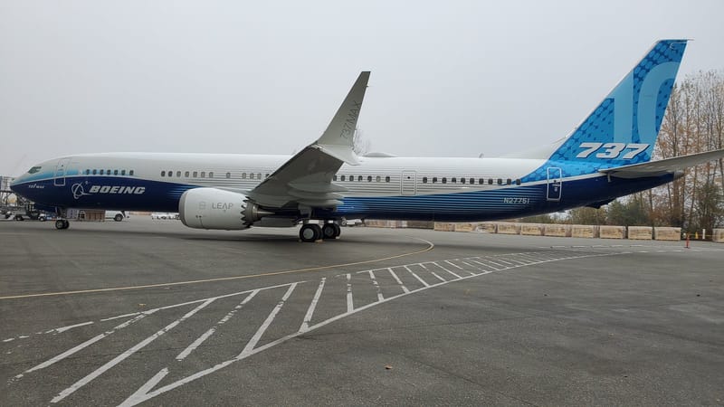Boeing 737-10 de fuselagem branca e azul, com a marca Boeing, parado em pátio de pista sob céu nublado