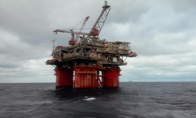 Plataforma de petróleo com estrutura vermelha e guindastes, sobre o mar, sob céu nublado