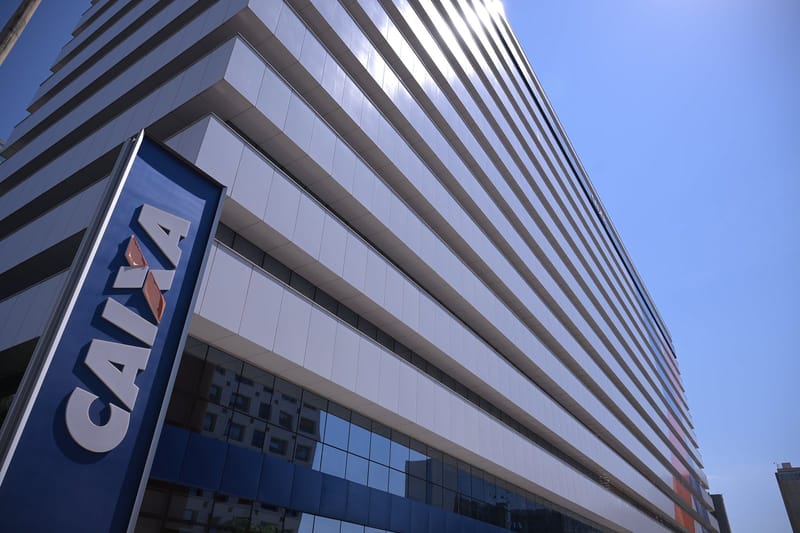 Placa azul com o logotipo da Caixa na entrada de um edifício comercial de fachada clara