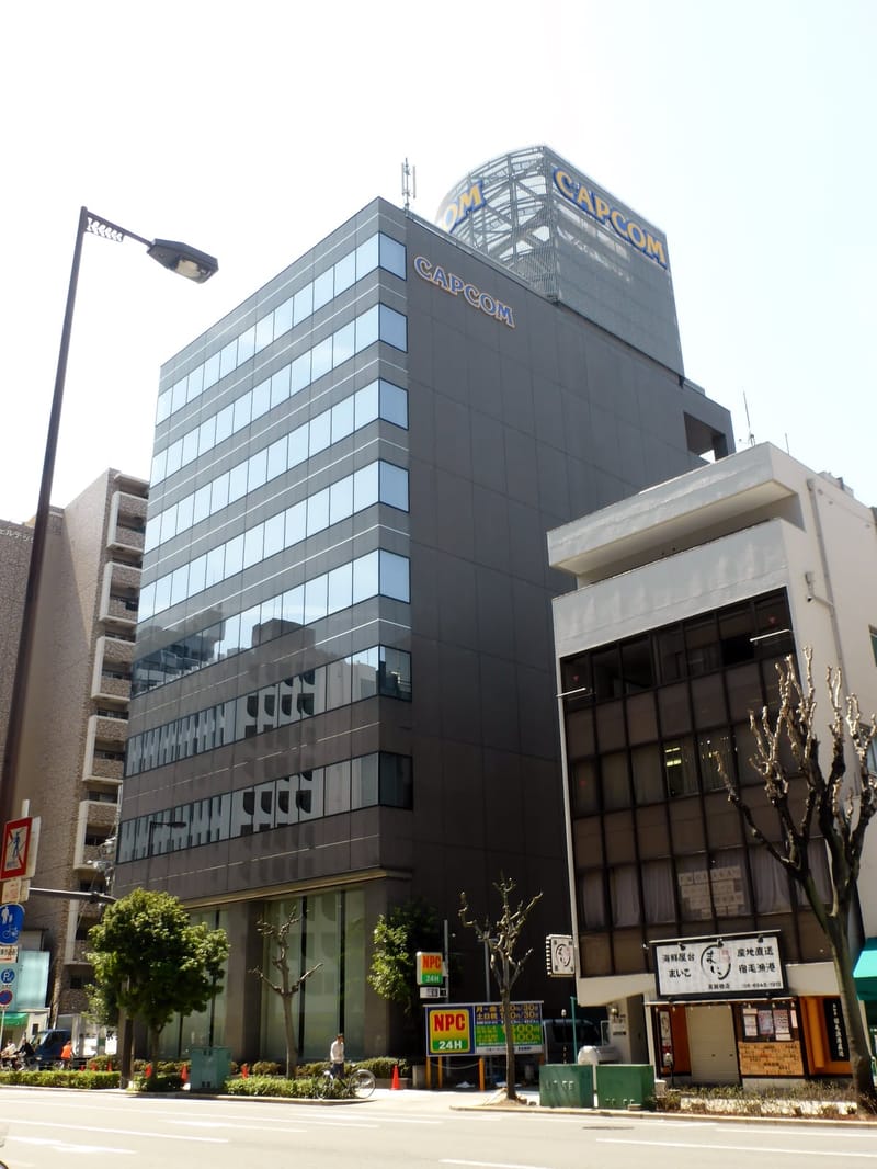 Prédio de escritórios de vidro e concreto com o logotipo da Capcom na fachada e no topo, sob céu claro