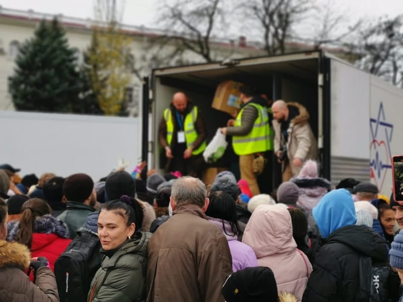 Voluntários de colete amarelo descarregam caixas de um caminhão diante de moradores agasalhados que aguardam ajuda em Kherson