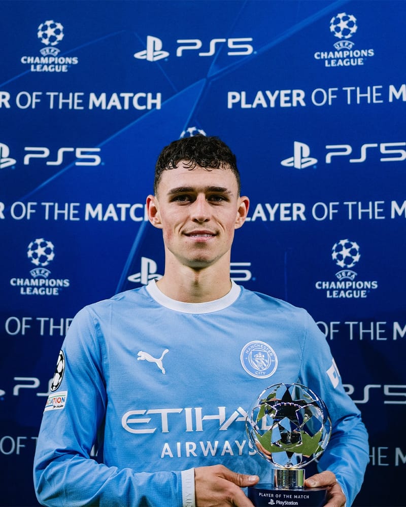 Phil Foden, de camisa azul-clara do Manchester City, sorri segurando o troféu de melhor jogador da partida na Champions
