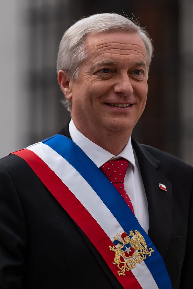 Retrato de José Antonio Kast, de terno escuro e gravata vermelha, com a faixa presidencial azul, branca e vermelha no peito, sorrindo