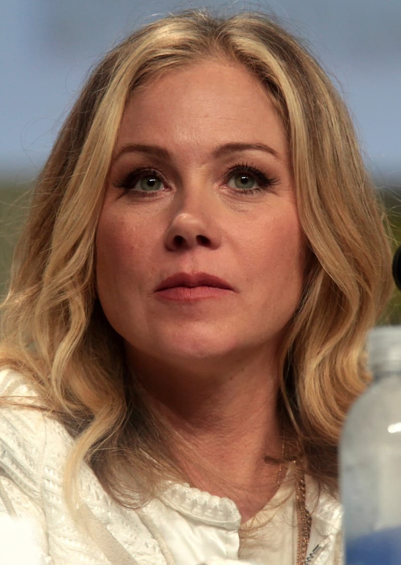 Christina Applegate, de cabelo loiro ondulado e blusa branca, olha para a frente durante painel