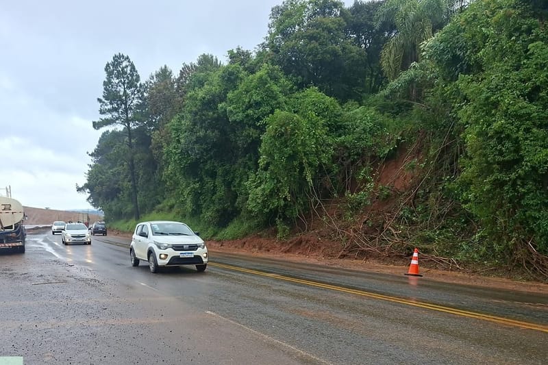 Encosta com terra solta ao lado de rodovia paranaense, com cone de sinalização e carros passando pelo trecho aberto