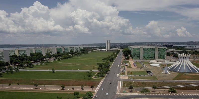 Vista aérea da Esplanada dos Ministérios, em Brasília, com os prédios dos ministérios e a Catedral, sob céu de nuvens