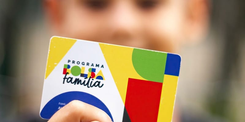 Cartão do Programa Bolsa Família erguido diante de uma criança desfocada