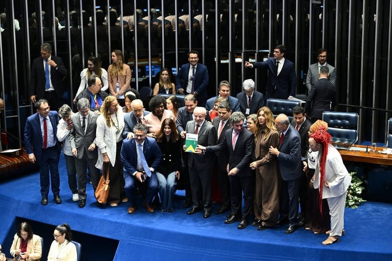 Lula segura um exemplar da Constituição cercado de parlamentares no plenário azul do Senado