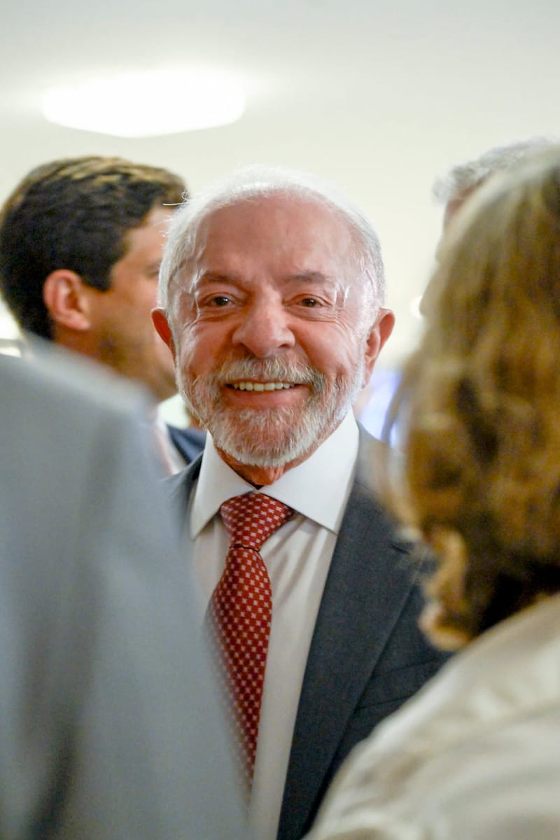 Lula, de terno cinza e gravata vermelha, sorri em meio a um grupo de pessoas