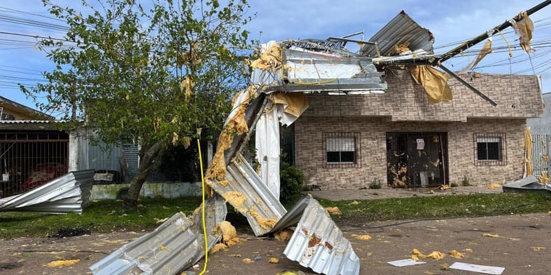 Casa de alvenaria com telhado de zinco arrancado e estruturas metálicas espalhadas pela rua e pelo gramado após vendaval