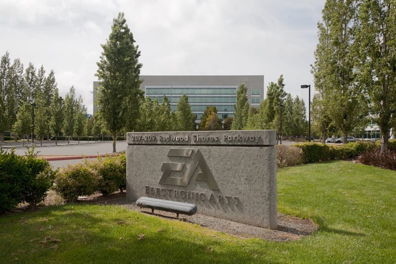 Placa de pedra com o logotipo da Electronic Arts num gramado, diante de um prédio de vidro cercado de árvores
