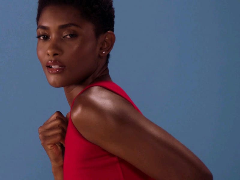 A atriz Erika Januza, de cabelo curto e vestido vermelho, olha para a câmera diante de um fundo azul