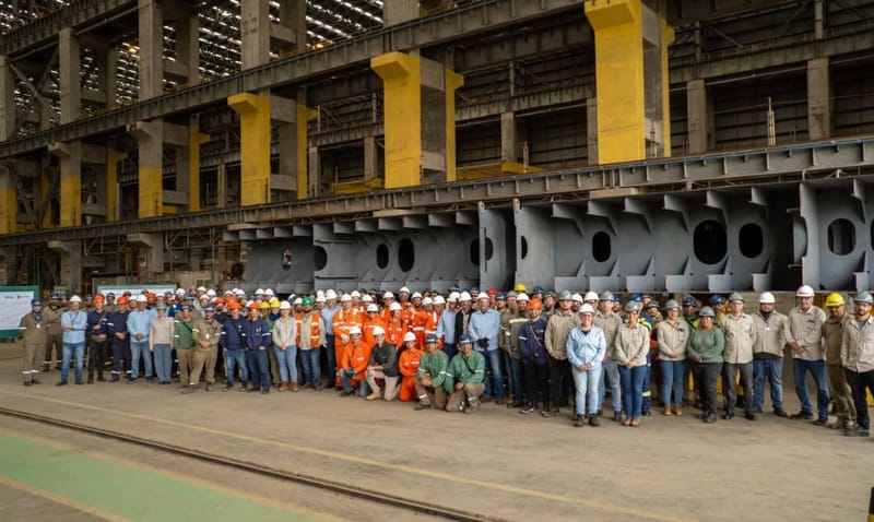 Dezenas de trabalhadores de capacete posam diante de grandes blocos de aço no galpão do Estaleiro Rio Grande, no Rio Grande do Sul
