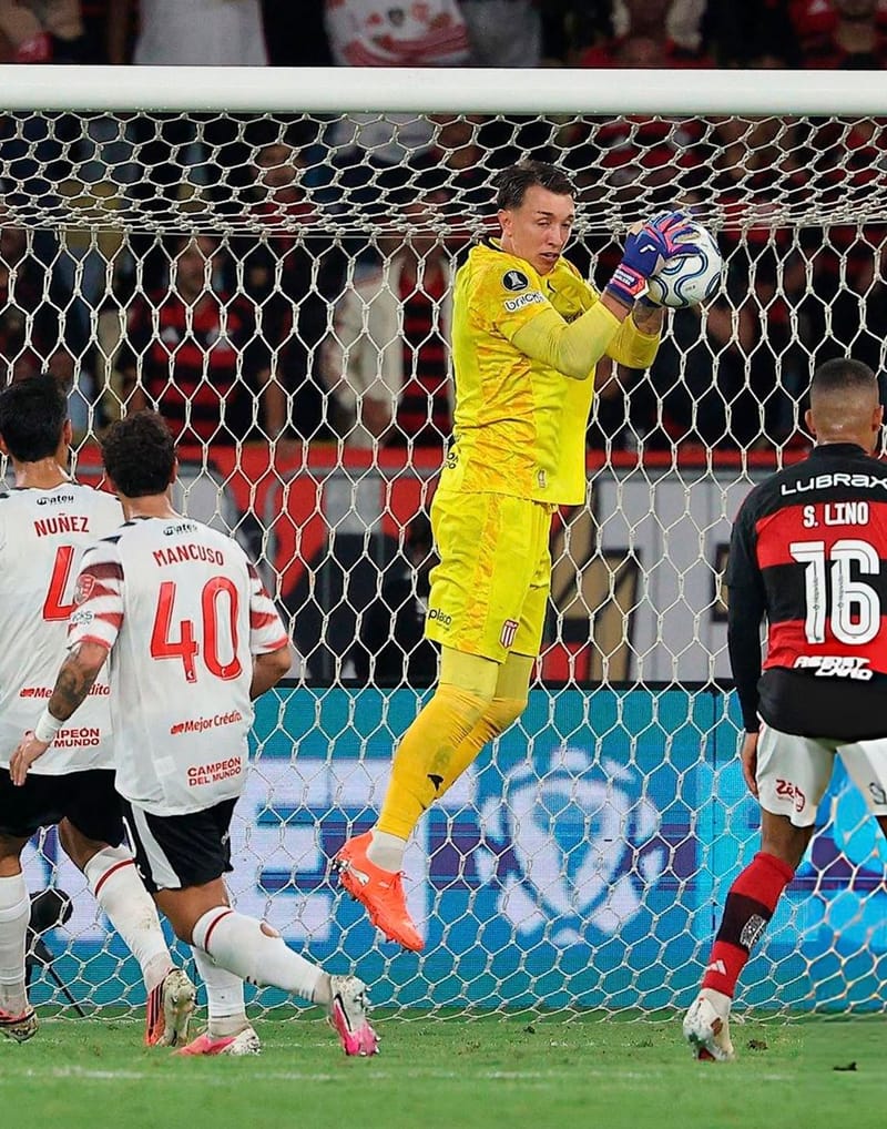 O goleiro Muslera, de amarelo, salta e agarra a bola em frente ao gol, com jogadores do Estudiantes e do Flamengo na área