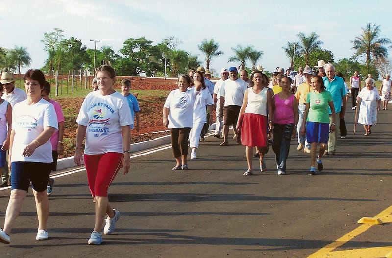 Grupo de idosos faz caminhada em avenida, de roupas esportivas, numa manhã de sol