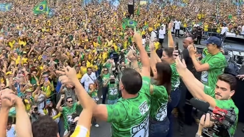 Do alto de um caminhão, Flávio Bolsonaro, de camiseta verde do Bloco do 22, ergue os braços diante de uma multidão de verde e amarelo com bandeiras do Brasil na Avenida Paulista