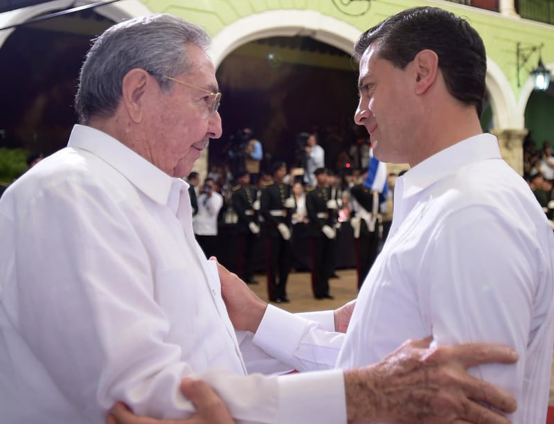 Raúl Castro, de cabelo grisalho e óculos, de camisa branca, cumprimenta com as mãos nos braços o então presidente mexicano, também de camisa branca, diante de uma guarda de honra
