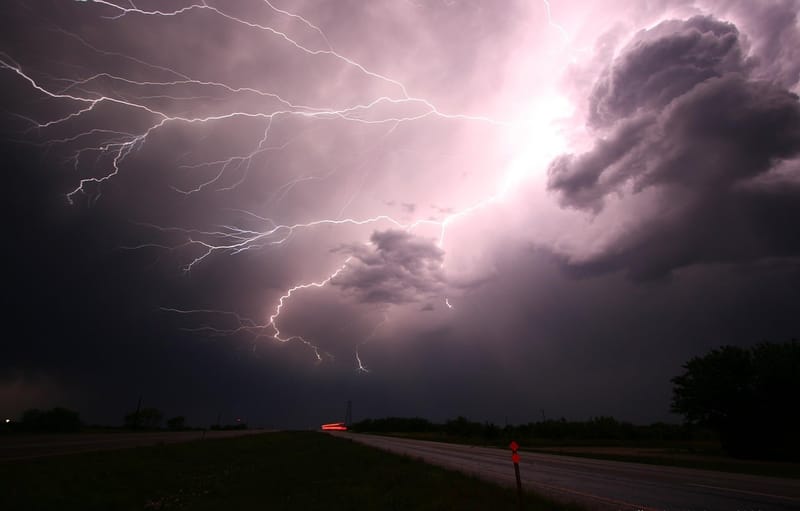 Raios riscam um céu escuro e carregado de nuvens sobre uma estrada de campo ao entardecer