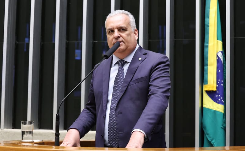 Alfredo Gaspar, de terno e gravata, fala ao microfone na tribuna do plenário da Câmara, ao lado da bandeira do Brasil