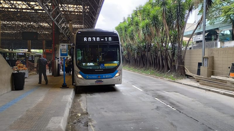 Ônibus branco e azul parado em plataforma de terminal de ônibus de São Paulo, com passageiros ao fundo