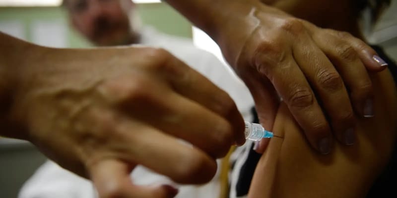 Mãos de um profissional de saúde aplicam uma injeção no braço de uma pessoa