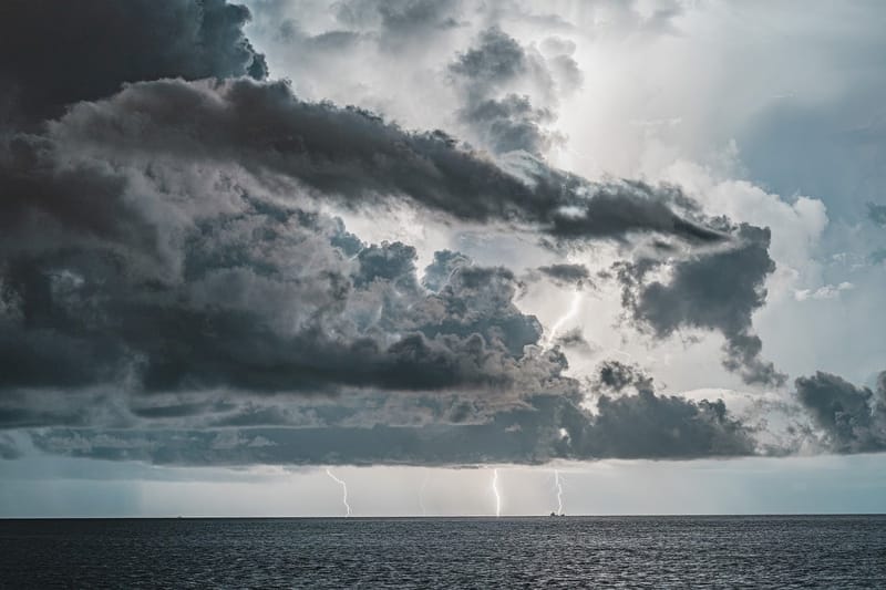Nuvens de tempestade carregadas sobre o mar, com três raios caindo no horizonte