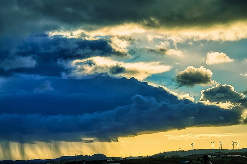 Céu com nuvens escuras de tempestade, chuva caindo ao longe e pôr do sol amarelo no horizonte