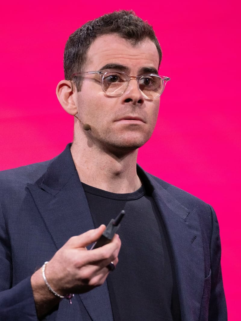 Adam Mosseri, chefe do Instagram, de óculos e paletó escuro, fala com um microfone de headset diante de um fundo rosa