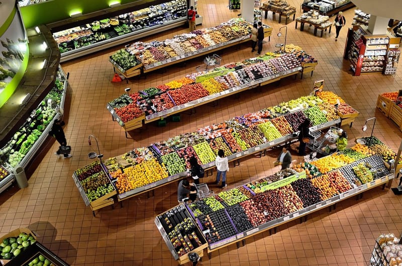 Corredores de frutas e verduras de um supermercado vistos de cima, com clientes e carrinhos entre as bancas