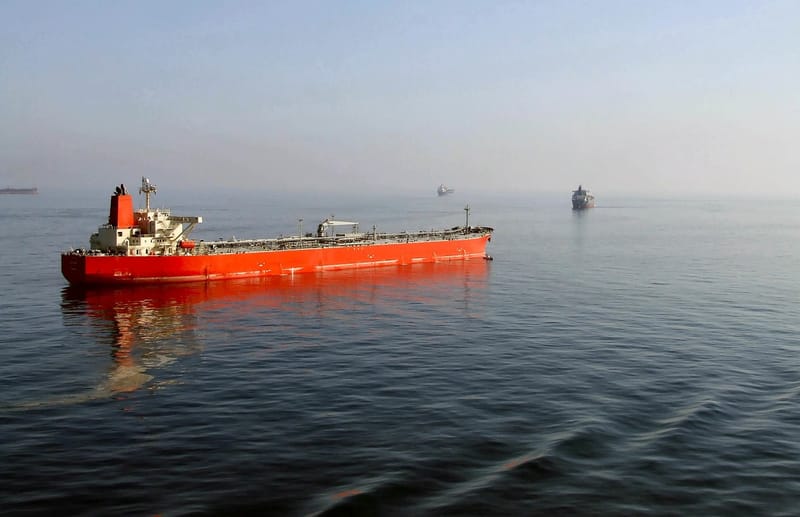 Petroleiro de casco vermelho em mar calmo no Estreito de Ormuz, com outros navios ao fundo na neblina