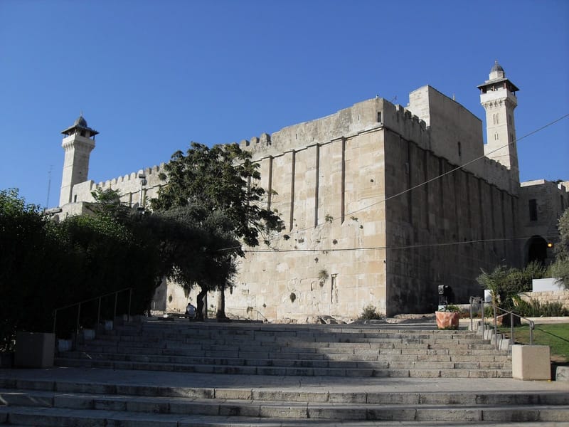 Fachada de pedra do Túmulo dos Patriarcas, com dois minaretes, vista de uma escadaria em Hebron, sob céu azul