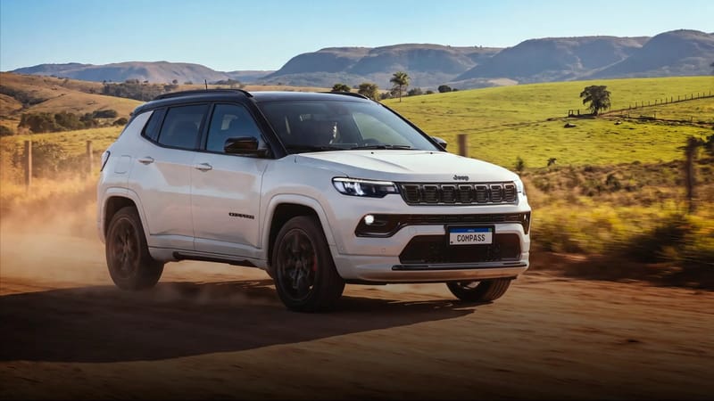 SUV Jeep Compass branco com teto preto rodando em estrada de terra, com pastos e morros ao fundo